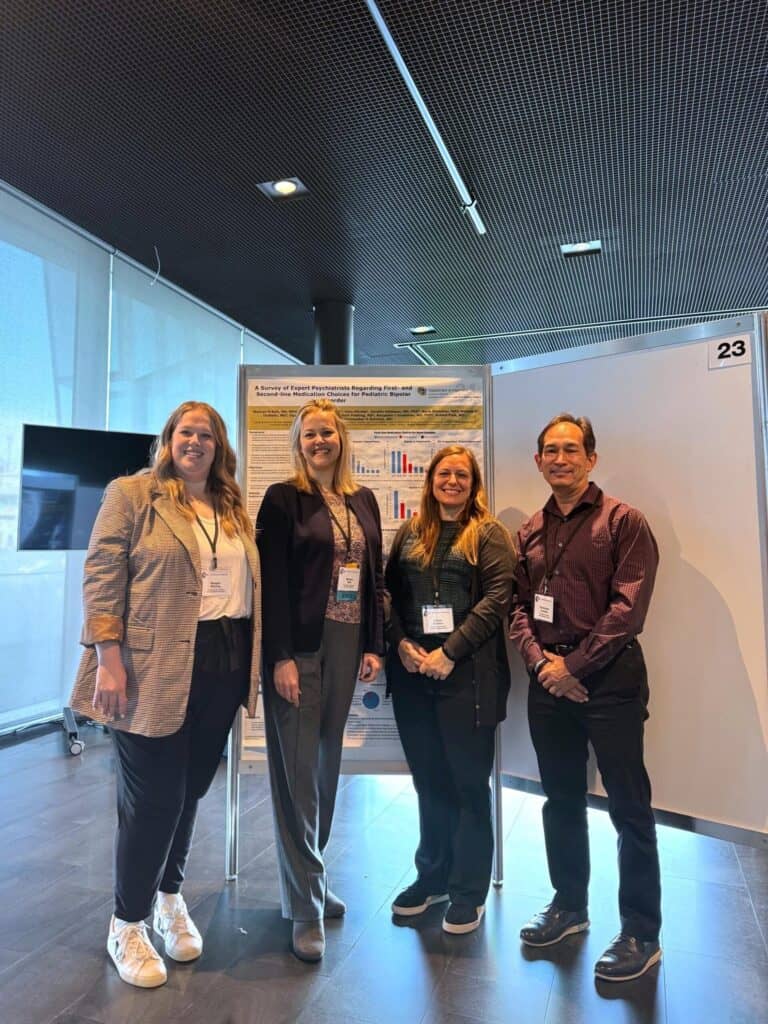 Four people stand smiling in front of a research poster with charts.