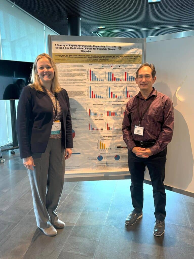 Two people stand smiling in front of a scientific research poster