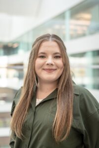 Emerald Saldyt, Professional Research Associate, in a green button-down shirt with a blurred office background