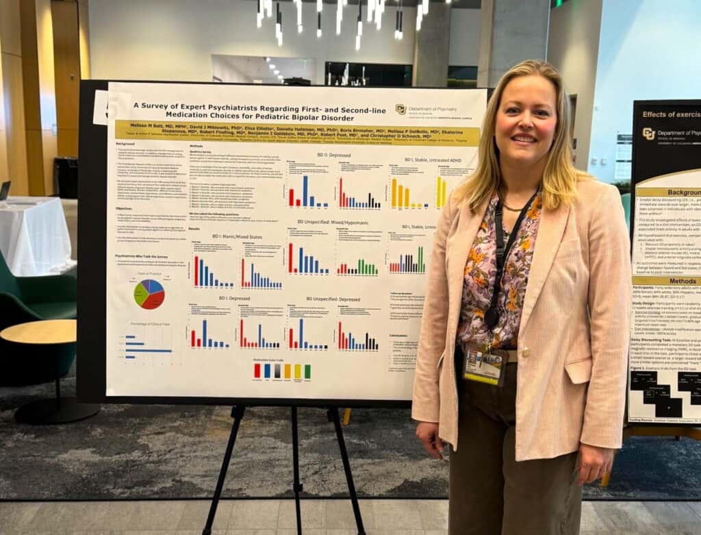 A woman stands smiling beside a research poster