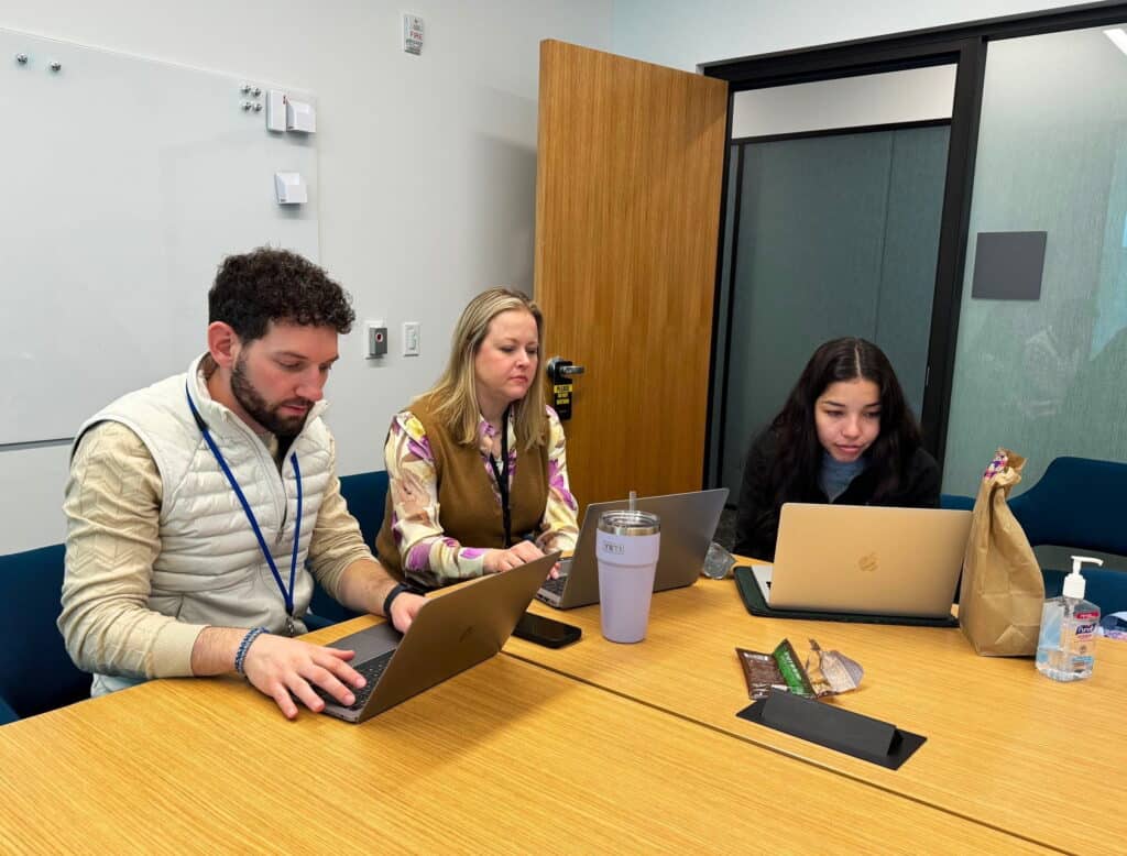 Three people work at a wooden conference table,