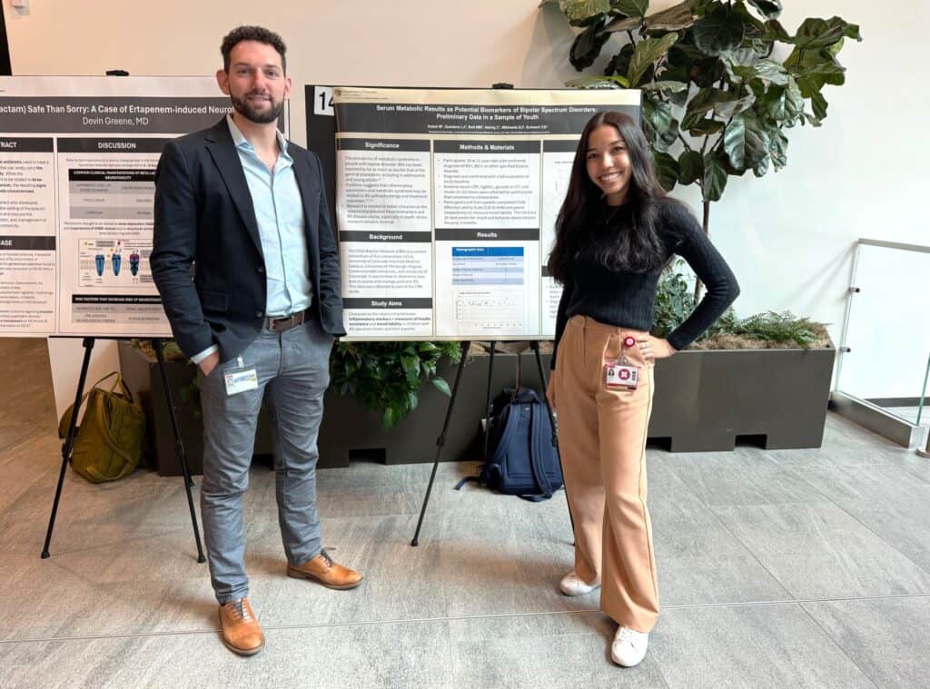 A man and woman stand smiling beside research posters indoors.