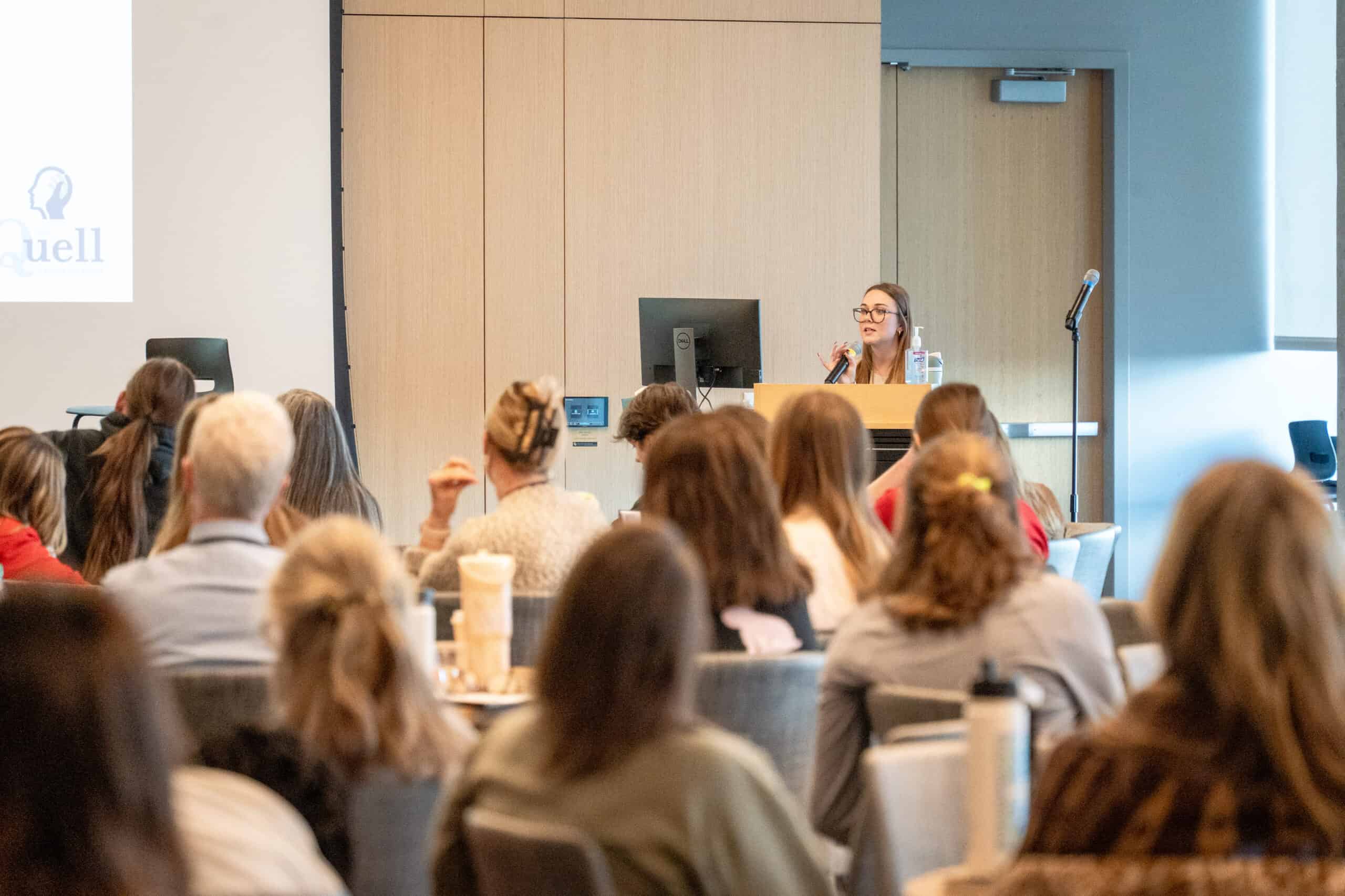 an event speaker at a podium with a room full of people